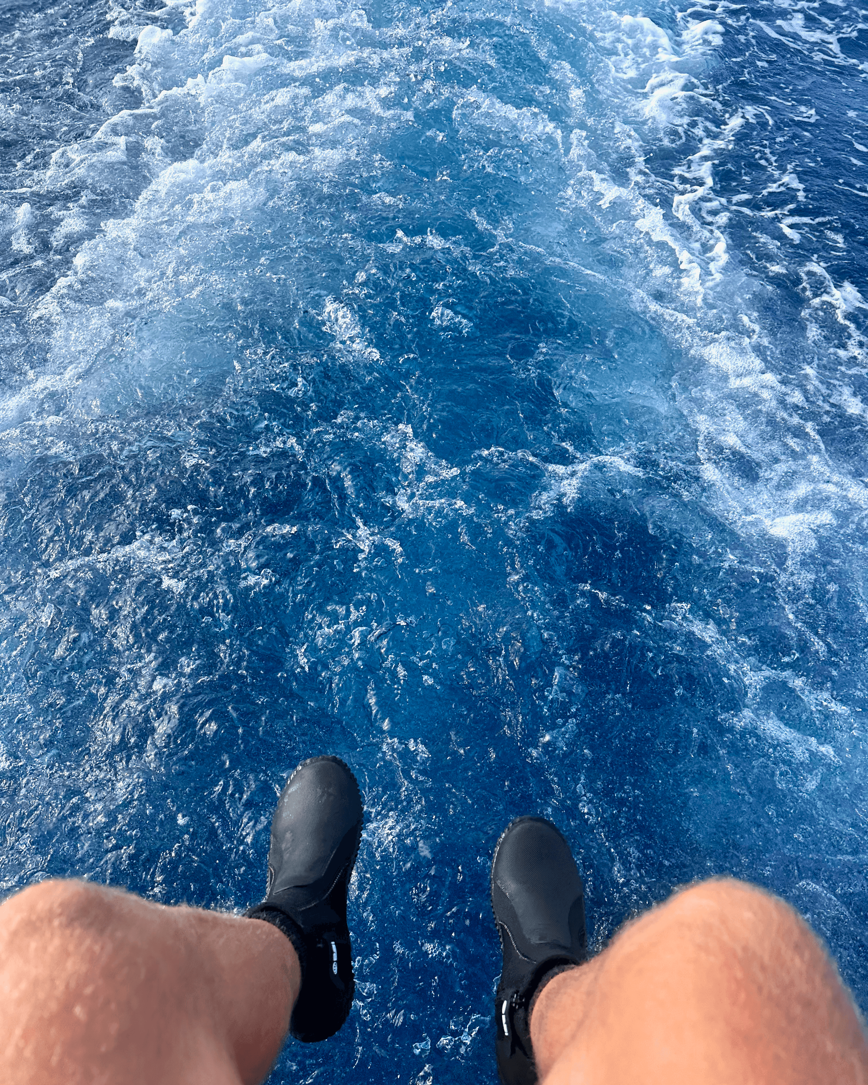 Feet hanging off the back of a SCUBA diving boat with blue ocean